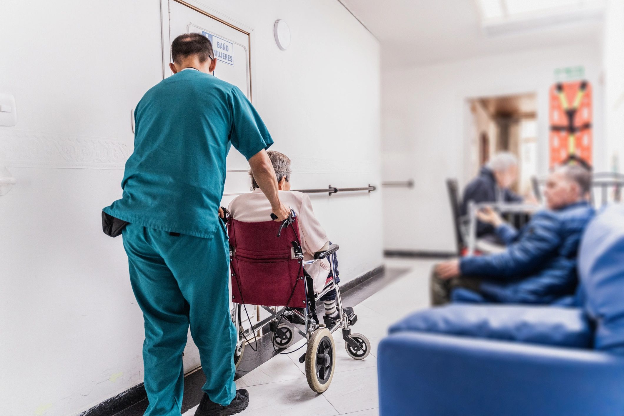 Caregiver pushing a senior woman in a wheelchair in a care facility corridor